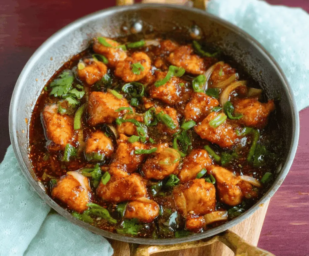Spicy Indian Chili Chicken served with fresh herbs and vibrant red chili peppers, garnished with chopped green onions.