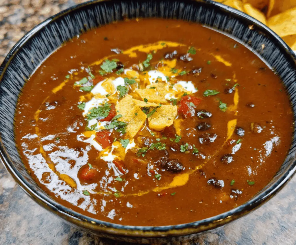Hearty Mexican Style Black Bean Soup garnished with chopped cilantro and lime wedges, served in a bowl with colorful toppings.