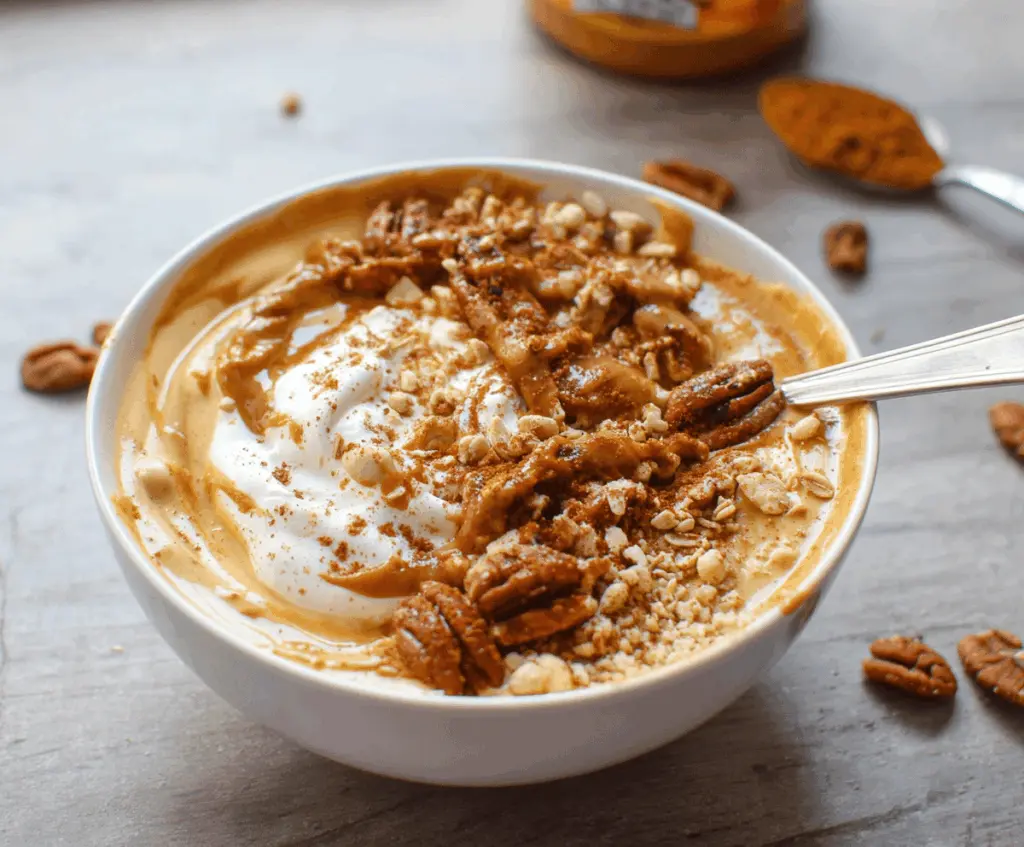 Creamy pumpkin pie yogurt bowl topped with whipped cream, cinnamon, and pumpkin seeds for a healthy fall breakfast